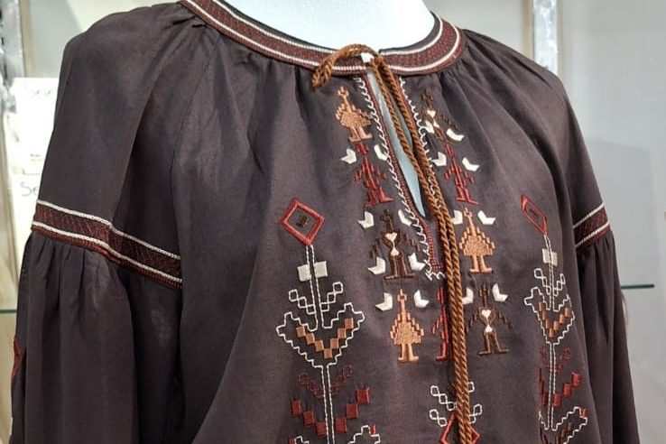 Detaj i qëndisjes tradicionale në një bluzë kafe prej liri