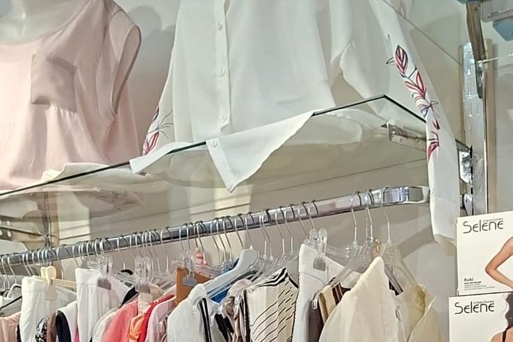 Këmisha të bardha në raft xhami mbi rafte veshjesh në butik